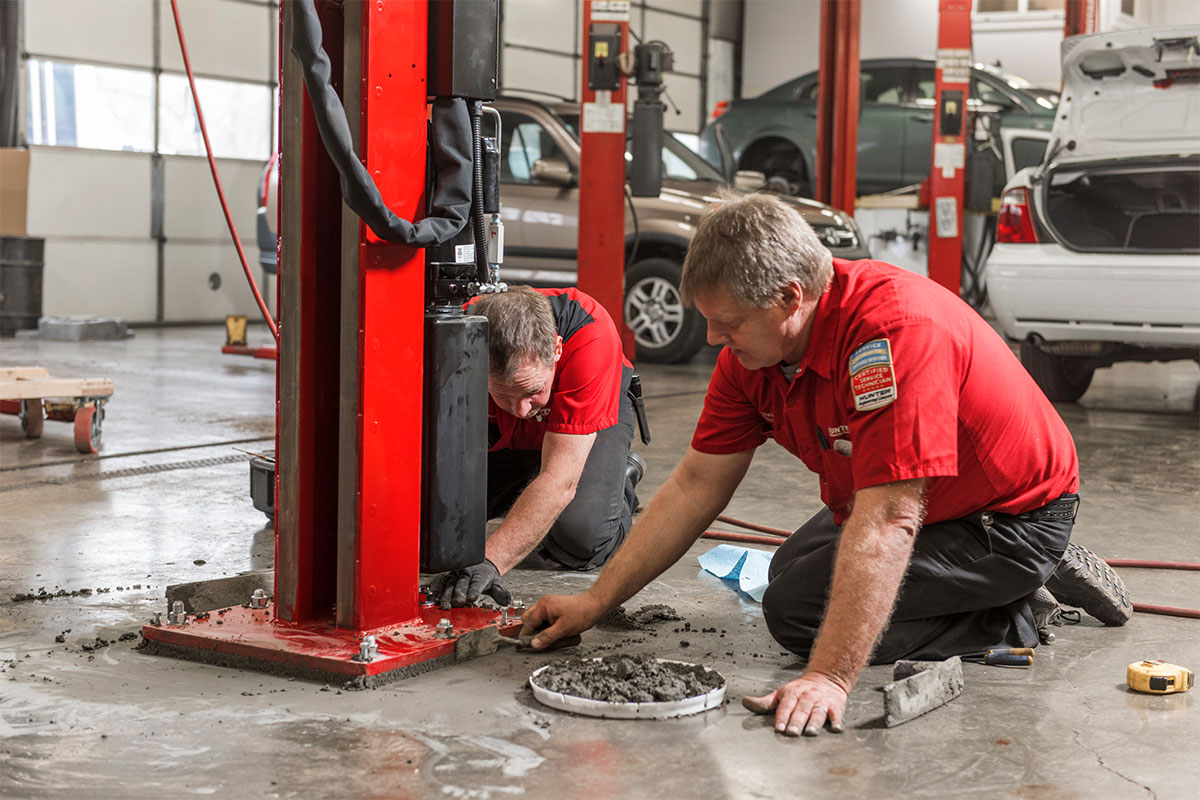 service reps using cement to mount four post lift