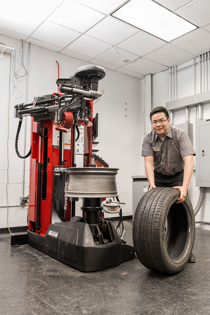 operator smiling at camera while rolling tire next to revolution tire changer